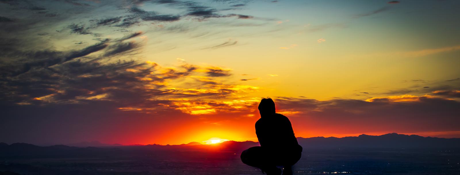 The silhouette of a young man as the sun crosses the horizon